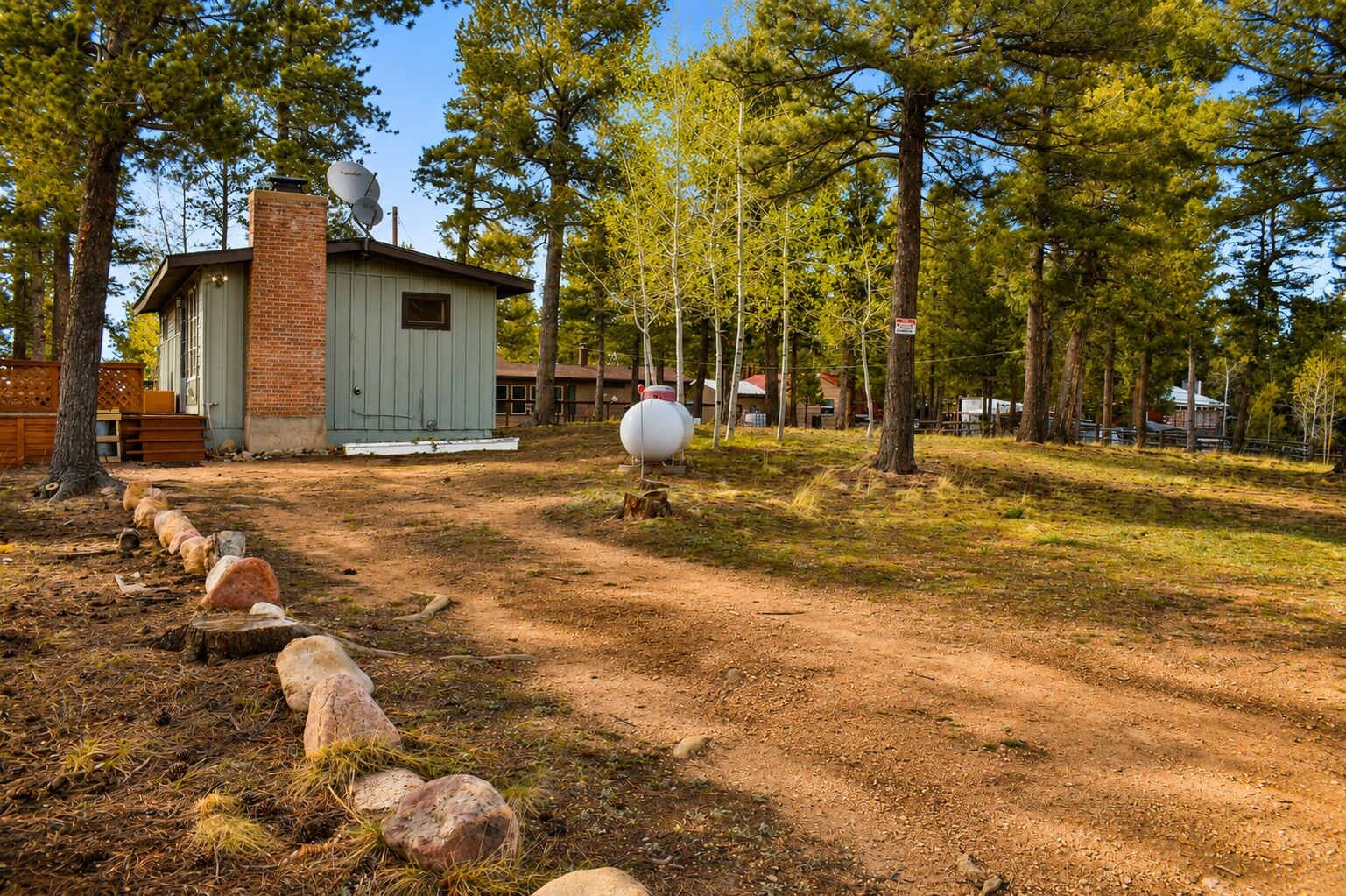 Una cabaña rústica con antena parabólica, rodeada por un área boscosa con un sendero de tierra y un objeto esférico blanco de gran tamaño.