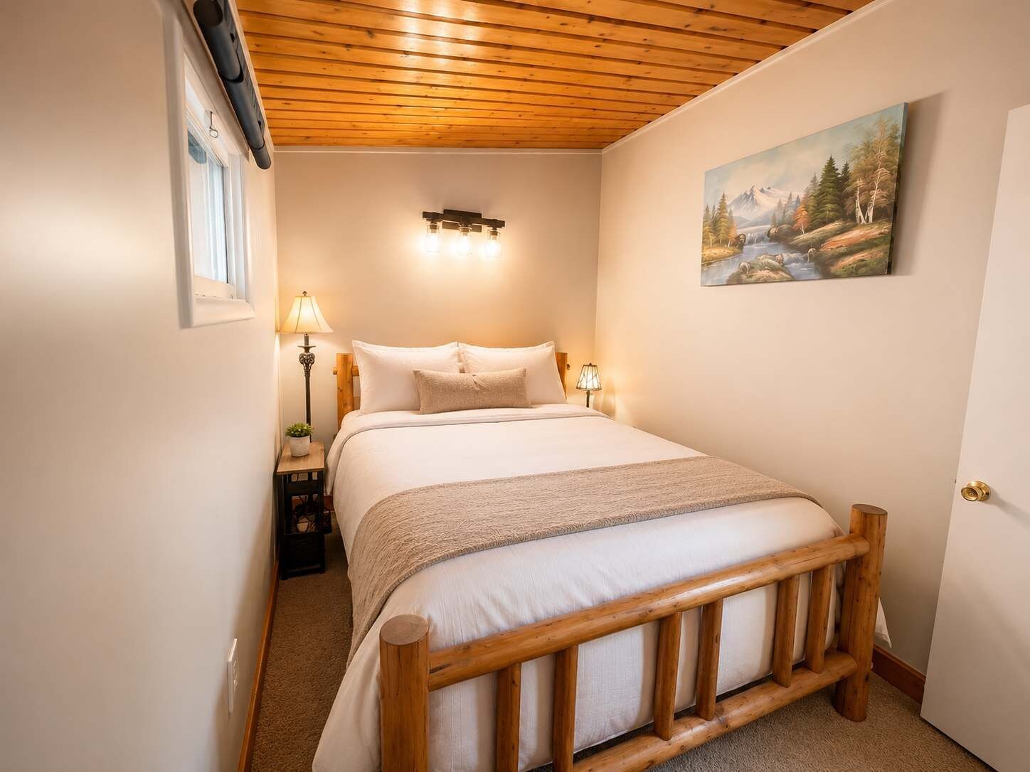 A bedroom with a wooden headboard, a bed with white bedding, two bedside lamps, a small bedside table with a lamp, and a painting on the wall.