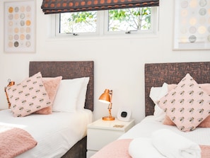 Un dormitorio con dos camas, cada una con cabecero, almohadas y mesita de noche con lámpara.
