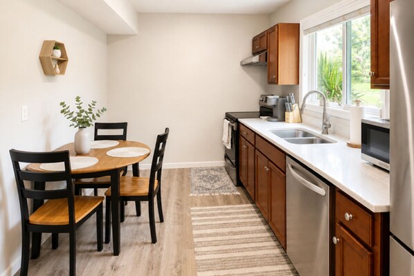 A modern kitchen with wooden cabinets, a stainless steel refrigerator, and a dining area with a wooden table and chairs.