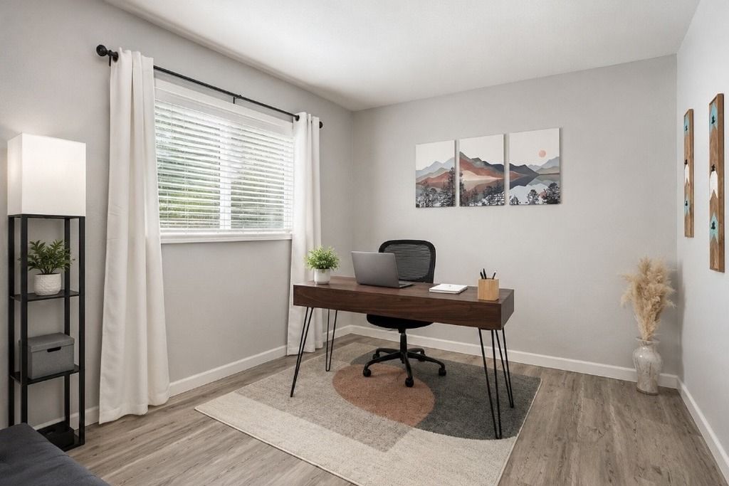A modern office space with a desk, chair, and laptop, a window with curtains, a plant, and artwork on the wall.