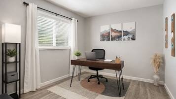 A modern office space with a desk, chair, and laptop, a window with curtains, a plant, and artwork on the wall.