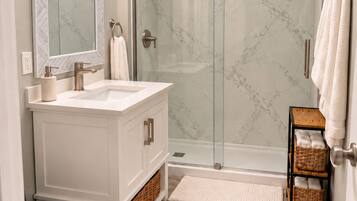 A modern bathroom with a glass shower enclosure, a white vanity, and a large mirror.