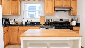 A kitchen with wooden cabinets, a stainless steel range hood, a dishwasher, and a coffee station.