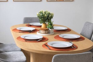 A round dining table with white plates, orange placemats, and silverware. There is a small potted plant in the center. - A Rare, Spacious Retreat - Downtown JC, Free Parking, Close to PATH (Jersey City)
