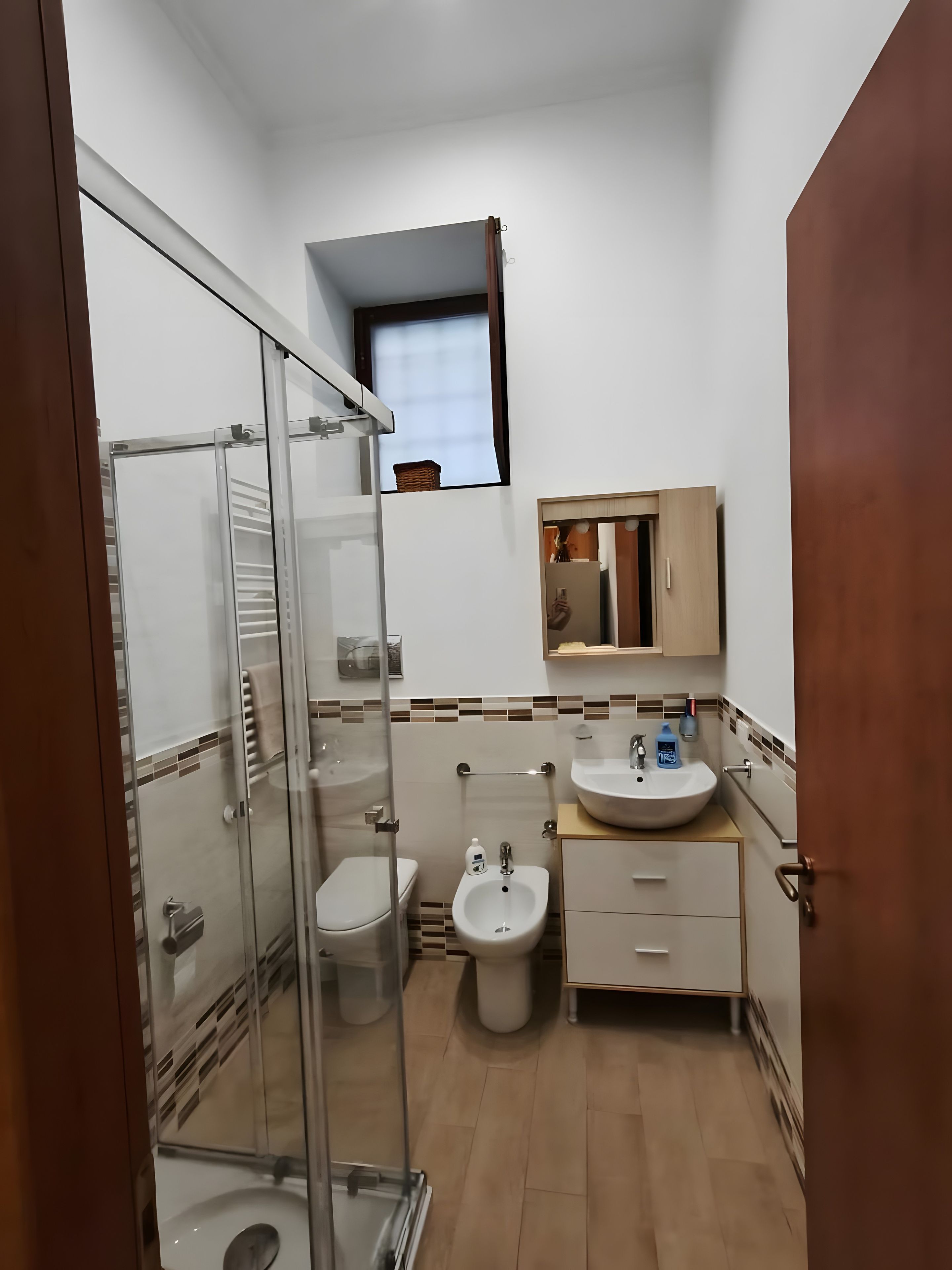 A compact bathroom with a glass shower enclosure, a toilet, a bidet, and a sink with a mirror above.