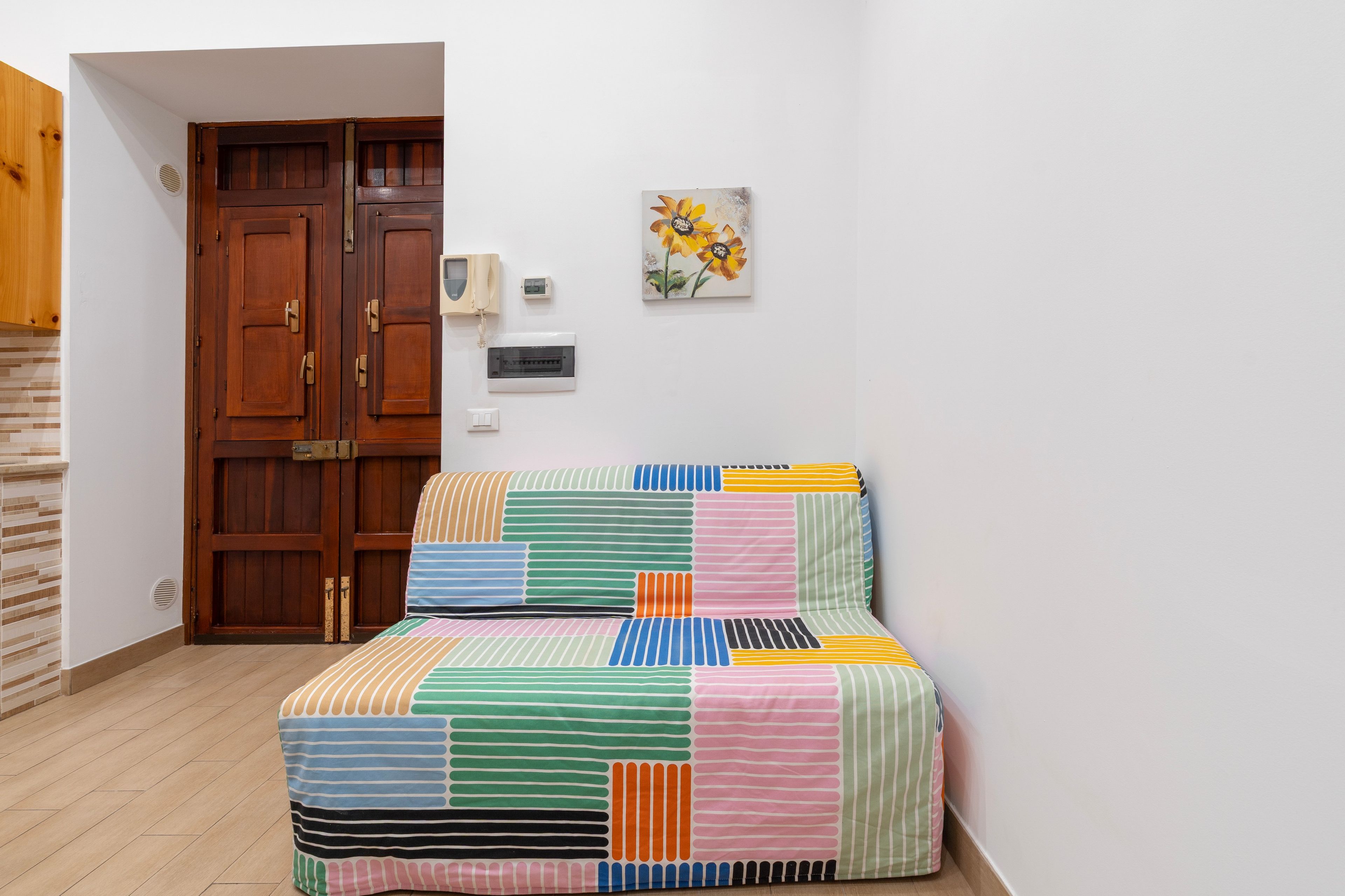 A room with a bed, wooden wardrobe, wall-mounted telephone, and a painting.