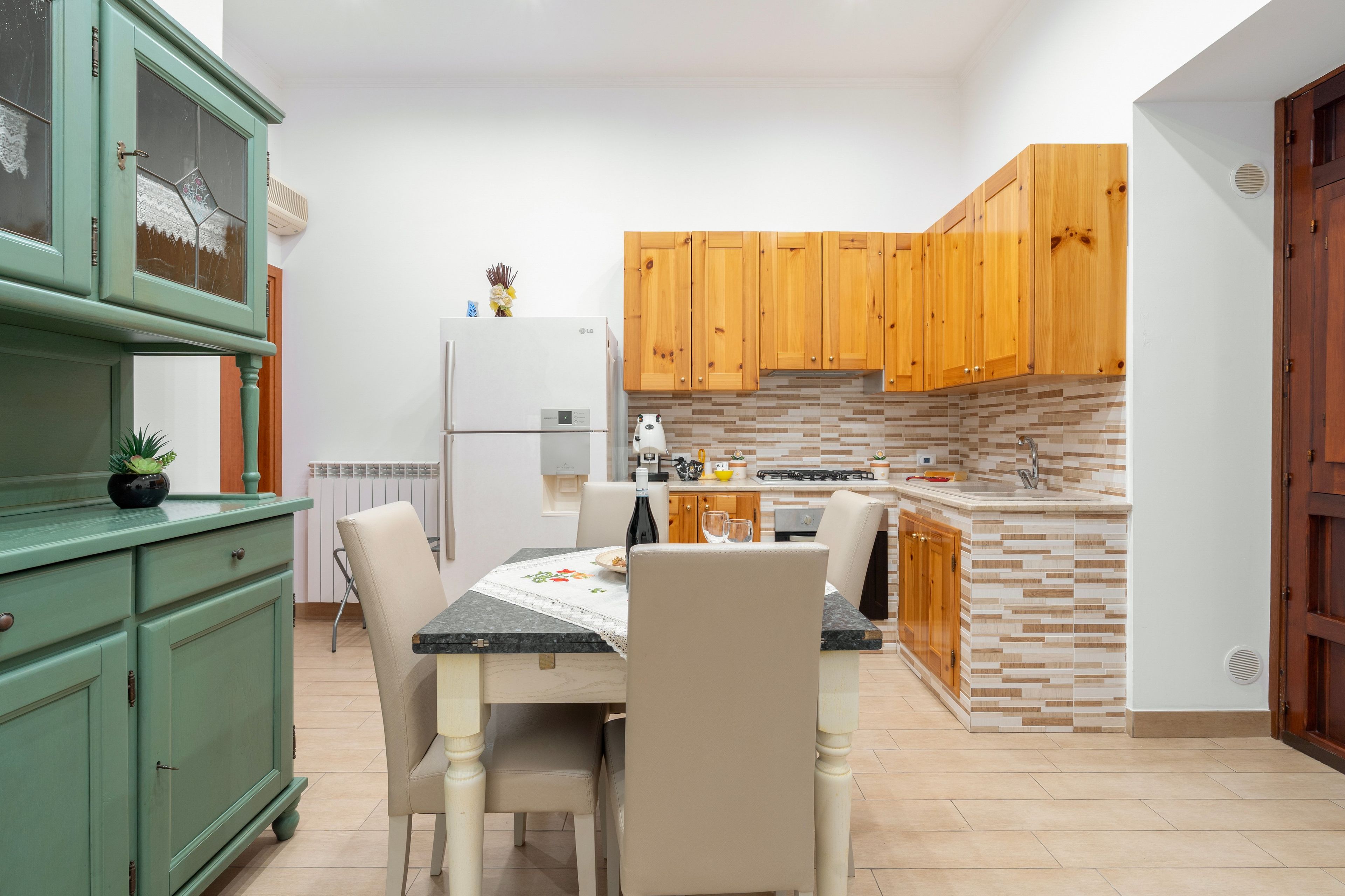 Une cuisine équipée d’une table à manger, de chaises, d’un réfrigérateur, de meubles de rangement en bois et d’un plan de travail recouvert de carreaux.