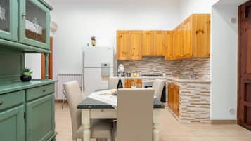 Une cuisine équipée d’une table à manger, de chaises, d’un réfrigérateur, de meubles de rangement en bois et d’un plan de travail recouvert de carreaux.