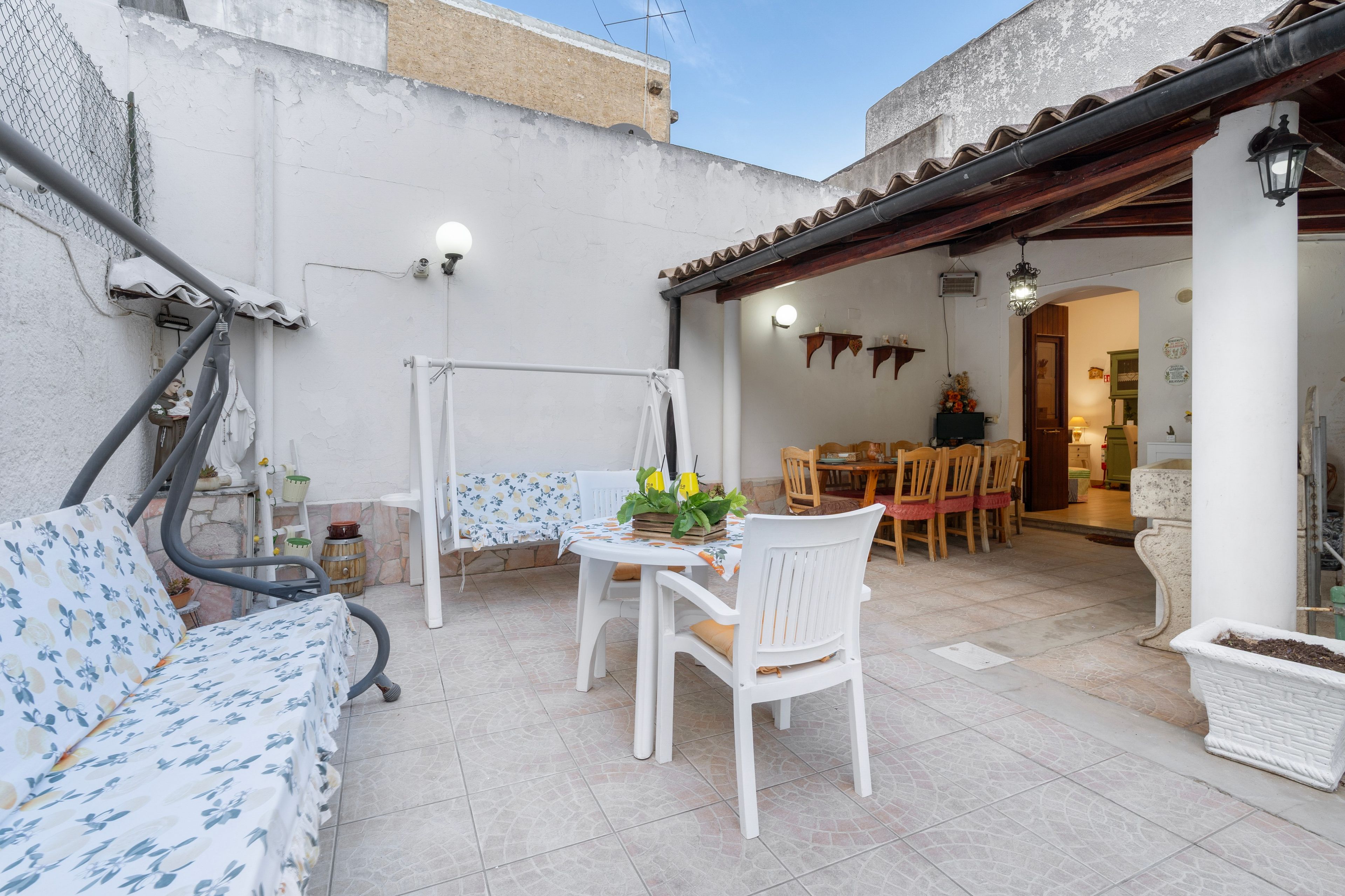 A patio with a white table and chairs, a white sofa, and a small garden area with a potted plant.
