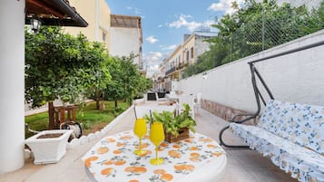 Une terrasse avec une table, deux chaises, un canapé et un pot de fleurs.