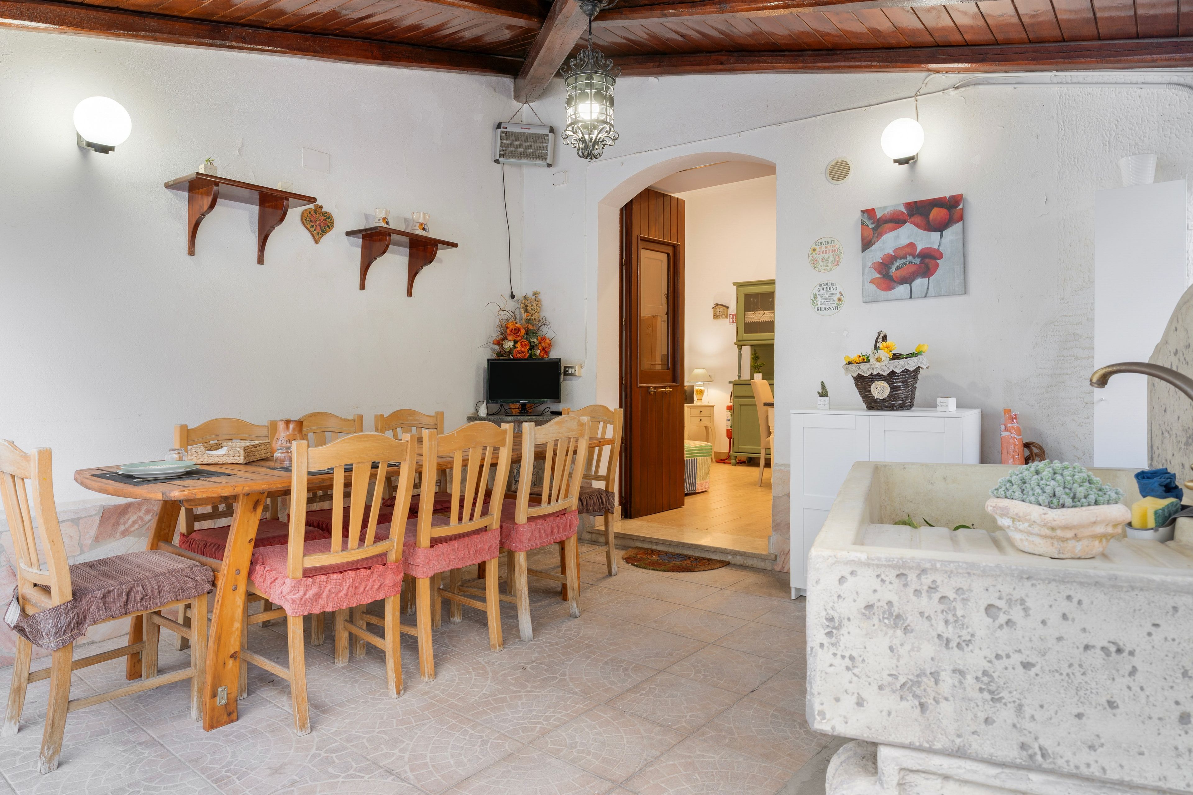 Un coin repas chaleureux avec des chaises en bois et une table, une cuisine équipée d’un évier et d’un plan de travail, et un espace de vie avec un canapé et des objets décoratifs.