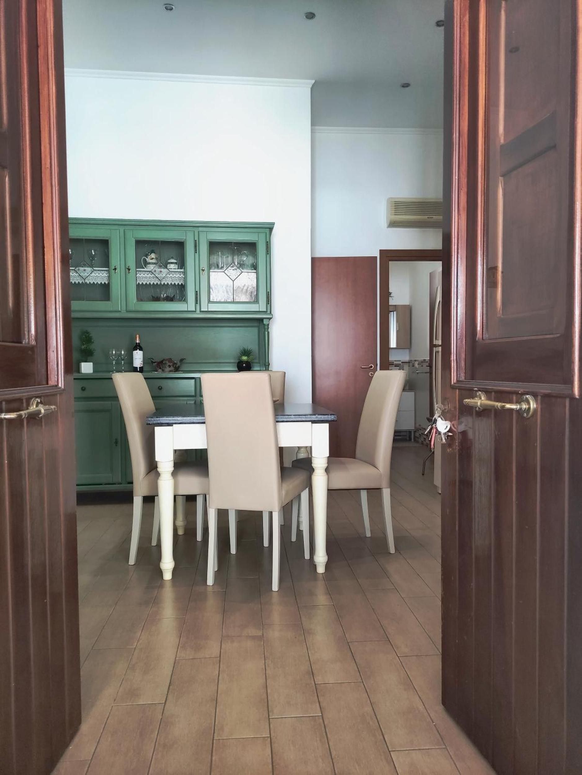 A dining area with a table and chairs, a green cabinet with glass doors, and a wooden door.