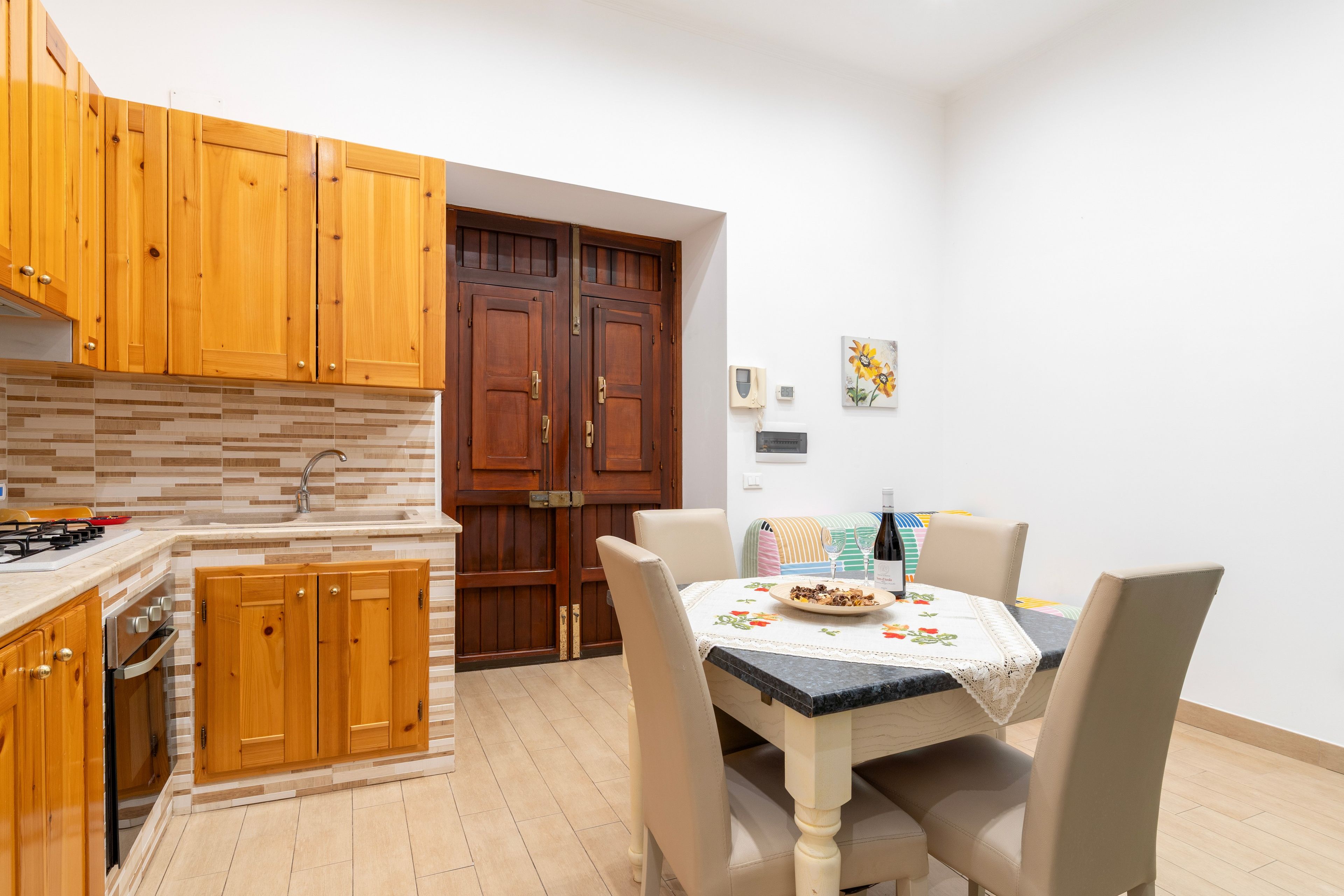 A compact kitchen with wooden cabinets, a tiled backsplash, and a dining area with a table set for two.