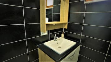 A bathroom with a white sink, black tiles, and a wooden cabinet above the sink.
