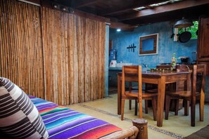 Une pièce avec un mur en bambou, une table à manger avec des chaises et une couverture colorée sur un lit.