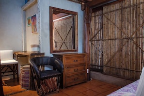 A room with a wooden wardrobe, a black leather chair, a wooden dresser, and a woven basket. - La Siesta Troncones    Beautiful Cozy Palapita (Troncones)