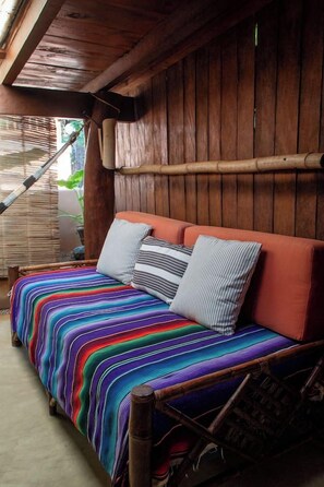 A wooden bed with a colorful striped bedspread and two pillows, set against a wooden wall with a bamboo structure to the side. - La Siesta Troncones    Beautiful Cozy Palapita (Troncones)