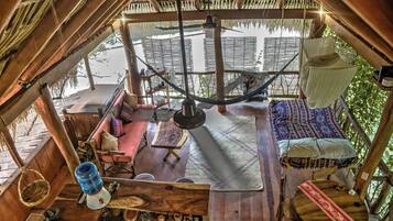 A wooden interior with a hammock, a sofa, a dining table, and a hanging light fixture.