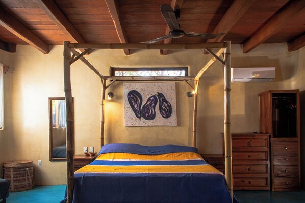 Ein Schlafzimmer mit Himmelbett, Deckenventilator, einem Fenster mit Tageslicht, einem Wandbild und Holzmöbeln.