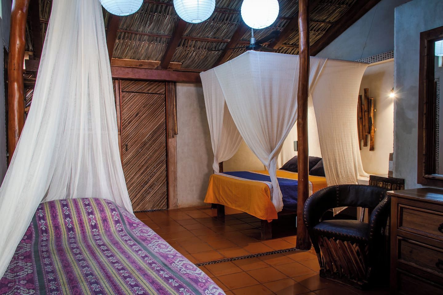 Una habitación con dos camas, cada una con dosel, una silla, una mesa y techo de madera.