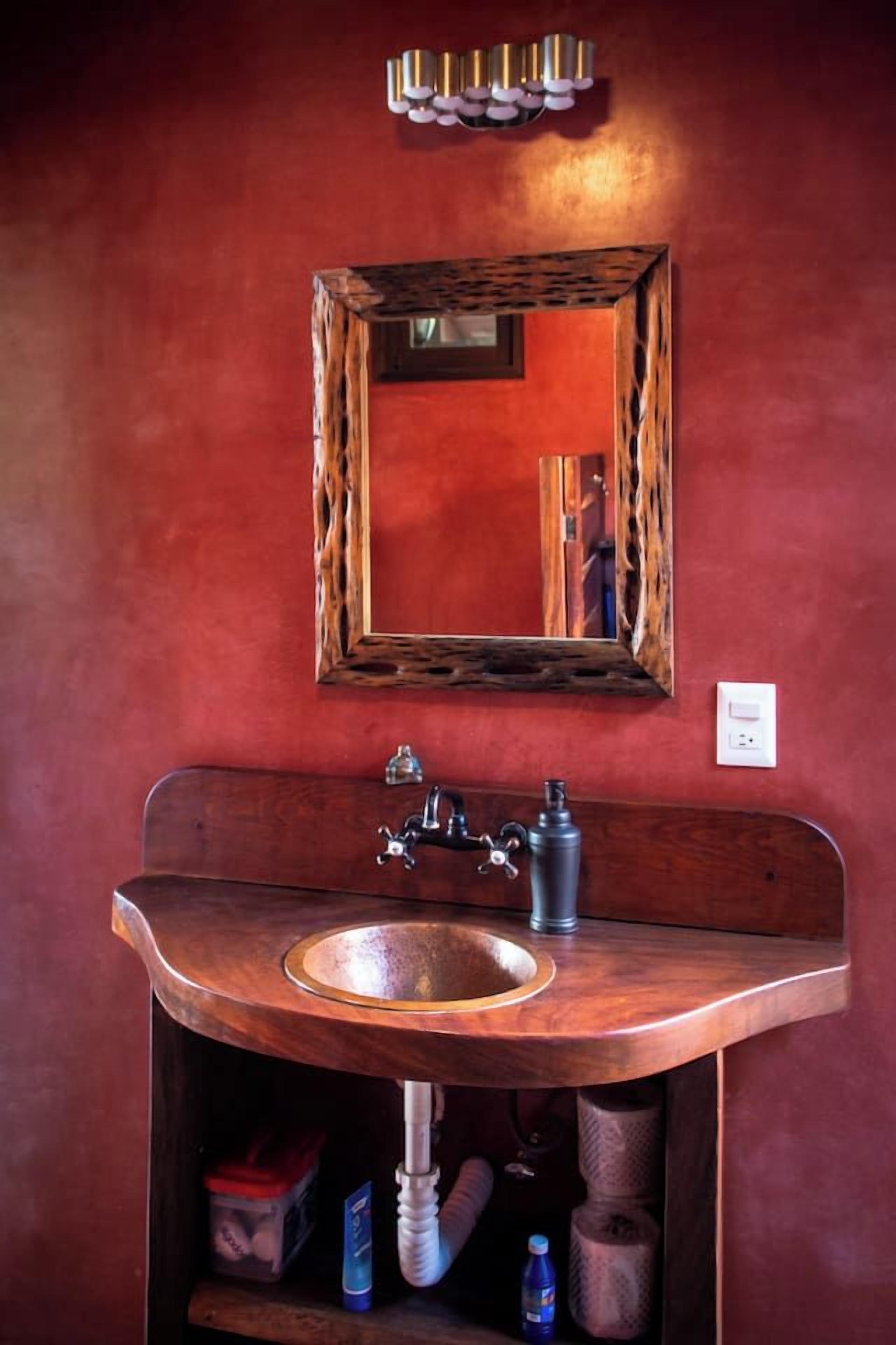 Un baño con tocador de madera, un espejo y un aplique en la pared.