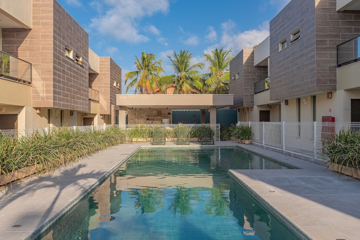 A swimming pool with a clear blue water surface, surrounded by a white fence and palm trees.
