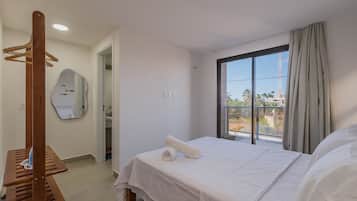 Ein Hotelzimmer mit einem Bett, einem Holz-Kleiderständer, einem Spiegel und einem Fenster mit Blick auf Palmen und einen Turm.