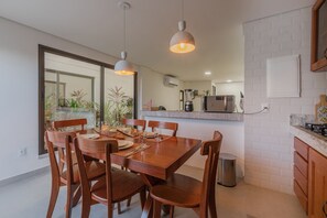 Un comedor con una mesa y sillas de madera, una cocina al fondo y vistas al exterior a través de un ventanal.