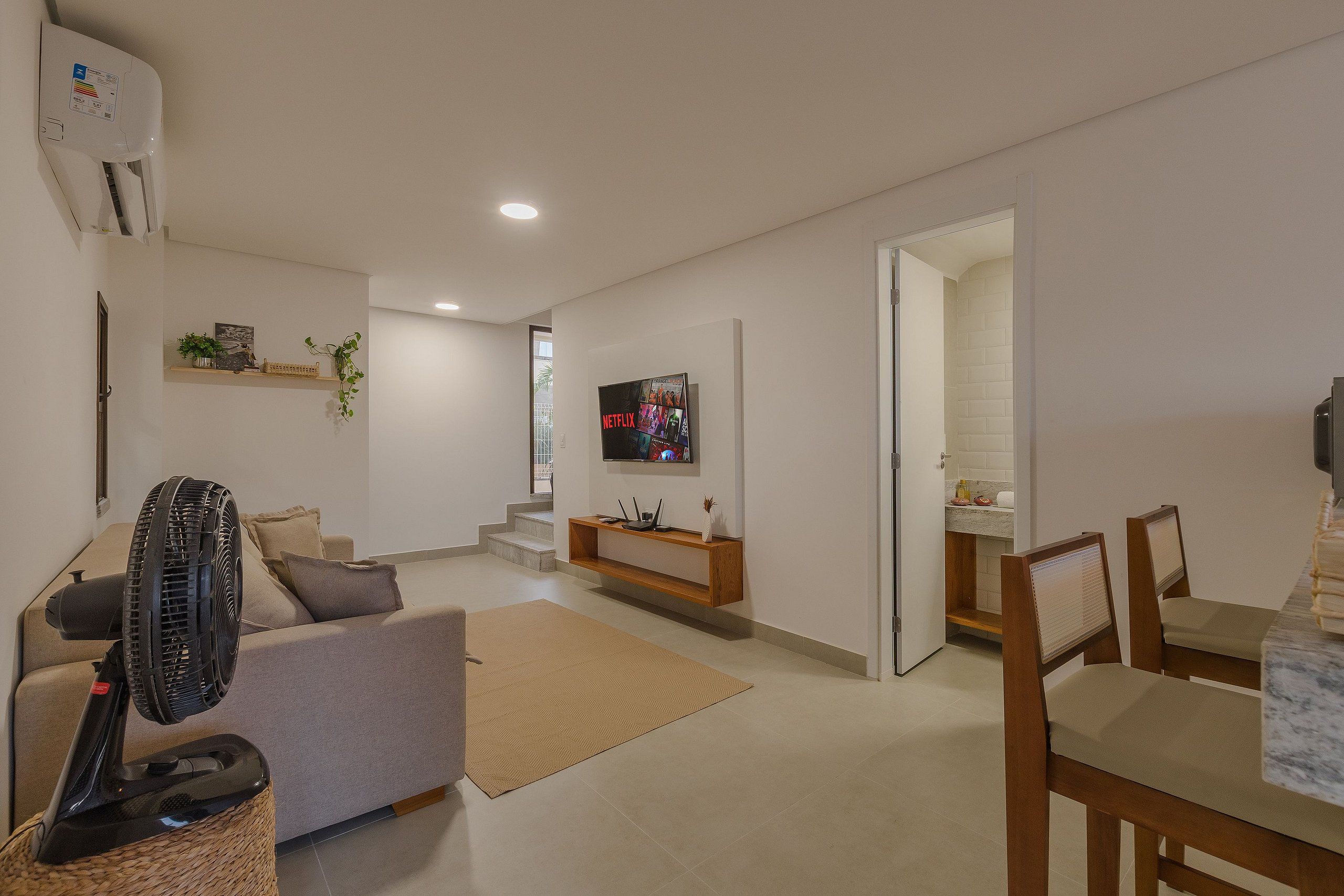 Ein modernes Wohnzimmer mit einer Couch, einem Ventilator, einem Fernseher und einer Treppe, die in einen anderen Raum führt.