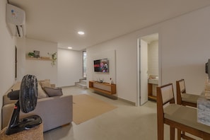 A modern living room with a sofa, a fan, a TV, and a staircase leading to another room.