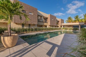Un edificio moderno con piscina, rodeado de palmeras y un jardín cuidado.