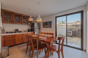 Une cuisine moderne avec des meubles en bois, une table à manger pour quatre personnes et une grande porte-fenêtre coulissante donnant sur un patio.