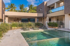 A modern outdoor pool area with lounge chairs and a covered seating area.