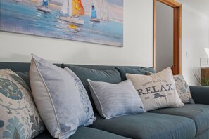 A living room with a sofa, two pillows, and a painting on the wall. - Harbor Hollow: Hot Tub>Fire Pit>Water Front>Game Room (Jay)