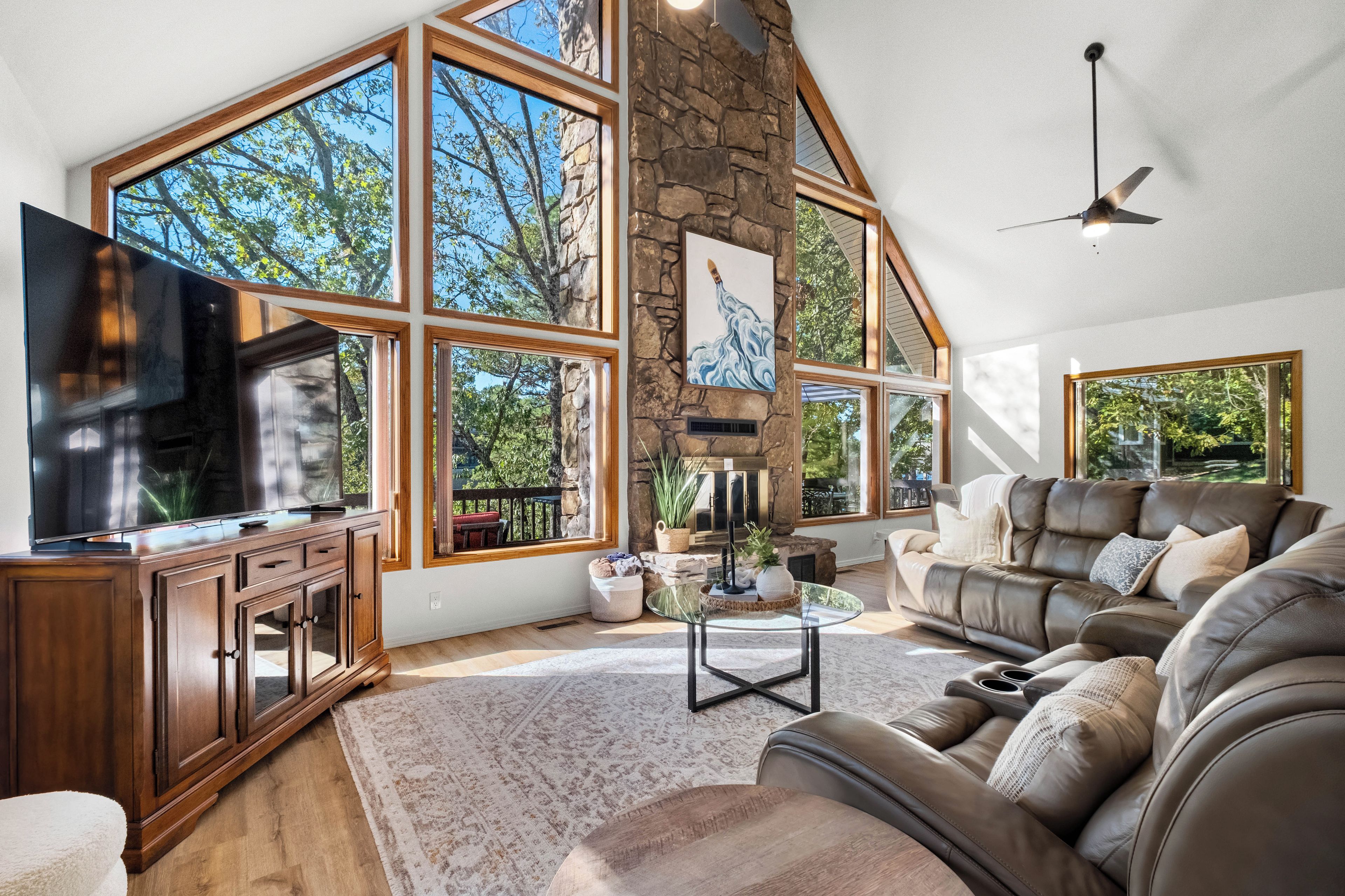A spacious living room with a large stone fireplace, a leather sofa, and a television on a wooden cabinet.