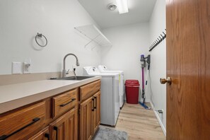 A compact kitchen with wooden cabinets, a sink, a washing machine, and a trash bin. - Harbor Hollow: Hot Tub>Fire Pit>Water Front>Game Room (Jay)