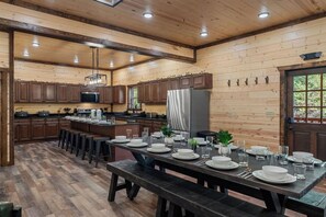 A spacious kitchen with wooden cabinets, a large island, and a dining area set for a meal. - New Luxury Lodge • Private Pool • Hot Tub • Game Room • Sleeps 18 (Sevierville)
