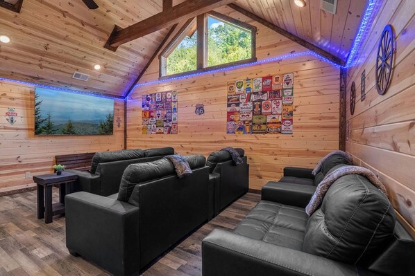 A log cabin interior with a seating area, wooden walls, a large window, and a wall decorated with various stickers. - New Luxury Lodge • Private Pool • Hot Tub • Game Room • Sleeps 18 (Sevierville)