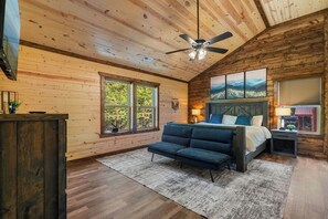 A bedroom with a bed, a sofa, a ceiling fan, and a large window. - Brand-New Luxury Cabin • Private Pool • Game Room • Sleeps 18 (Sevierville)