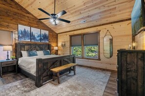 Une chambre avec un plafond en bois, un lit avec une banquette, un ventilateur de plafond et une grande fenêtre.
