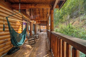 A wooden cabin with a porch, a hammock, rocking chairs, and a view of a forested hillside. - Brand-New Luxury Cabin • Private Pool • Game Room • Sleeps 18 (Sevierville)