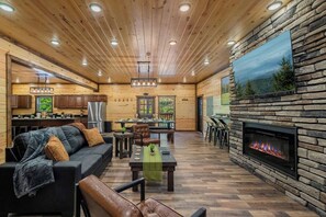 A spacious living area with a fireplace, wooden flooring, and a dining area. - Brand-New Luxury Cabin • Private Pool • Game Room • Sleeps 18 (Sevierville)