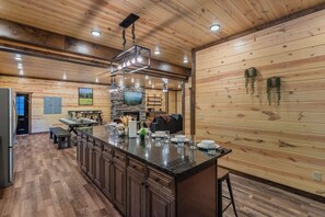 A spacious kitchen with a large island, wooden paneling, and a stone fireplace. - Brand-New Luxury Cabin • Private Pool • Game Room • Sleeps 18 (Sevierville)