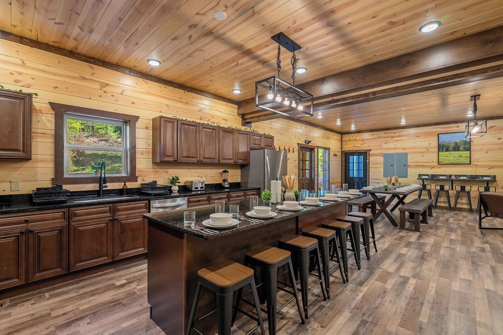 A spacious kitchen with wooden cabinetry, a central island with stools, and a view of the outdoors through a window.