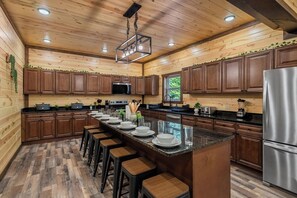 A spacious kitchen with wooden cabinets, a central island with stools, and modern appliances. - Brand-New Luxury Cabin • Private Pool • Game Room • Sleeps 18 (Sevierville)