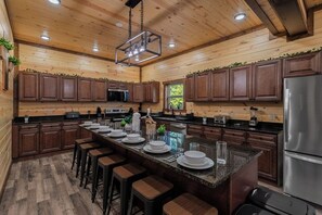 A kitchen with wooden cabinets, a central island with stools, and stainless steel appliances. - Brand New 18-Person Cabin | Private Pool, Theater & Game Room (Seviervill e)