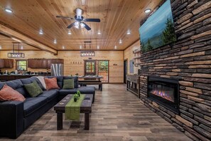 A spacious living area with a fireplace, a sofa, and a dining table. - Brand New 18-Person Cabin | Private Pool, Theater & Game Room (Seviervill e)