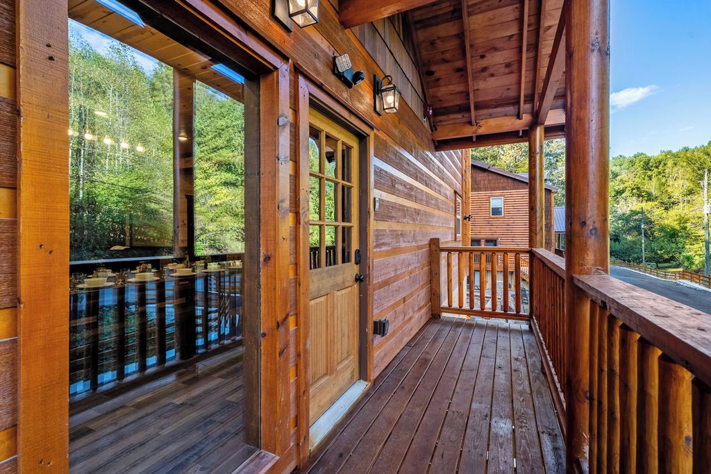 A wooden cabin with a porch, large windows, and a view of the forest.