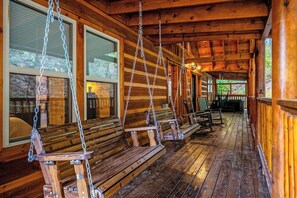 A wooden porch with swing seats and a view of the outdoors. - Brand New 18-Person Cabin | Private Pool, Theater & Game Room (Seviervill e)